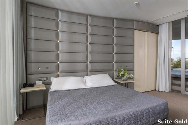Moderní ložnice s dvojlůžkem, elegantním čalouněným čelem a nočními stolky na obou stranách.