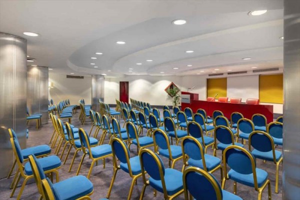 Konferenční místnost s modrými židlemi a červeným pódium.