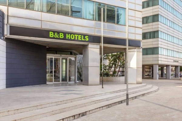 Vstup do hotelu B&B s šedou fasádou a prosklenými dveřmi.