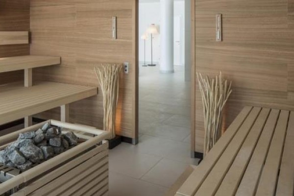 Moderní sauna s dřevěnými lavicemi a zásobníkem na kameny.