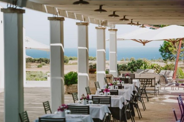 Venkovní restaurace s výhledem na moře a bílé stoly pod slunečníky.