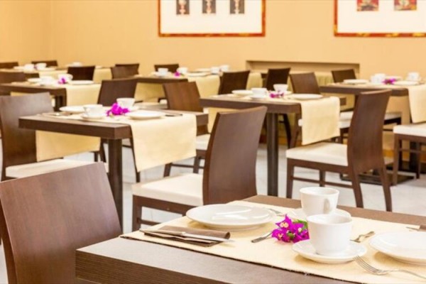 Elegantní restaurace s dřevěnými stoly, prostřenými bílým nádobím a dekorovanými květinami.