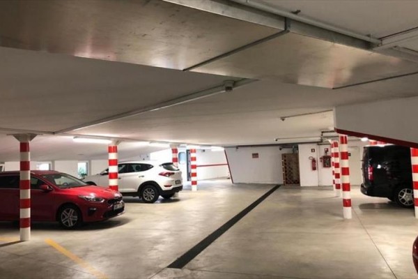 Podzemní parkoviště s několika zaparkovanými auty a sloupy s červenobílými pruhy.