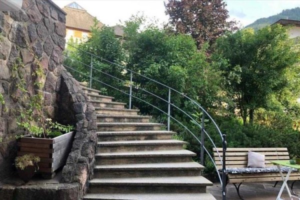 Exteriérové kamenné schodiště s kovovým zábradlím vedle lavičky a zeleně.
