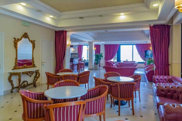 Elegantní hotelový salon s červenými křesly a závěsy.