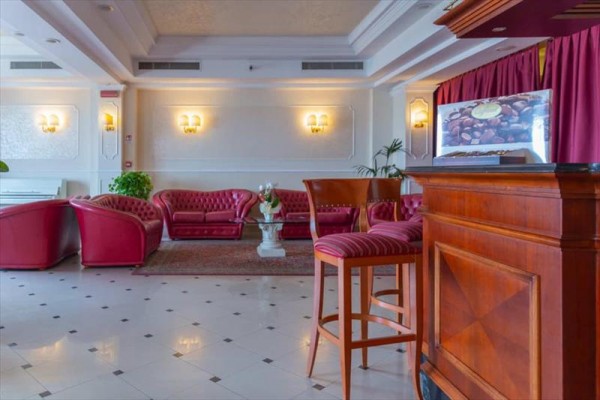 Elegantní hotelová lobby s červenými koženými křesly a pohovkami a dřevěným barem.