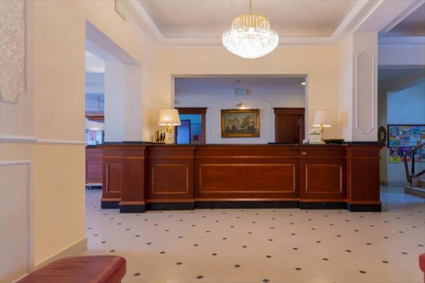 Recepce hotelu s dřevěným pultem a lustrem.