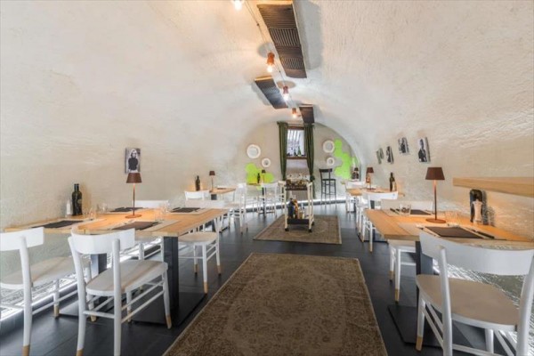 Stylová restaurace s bílými židlemi a dřevěnými stoly v klenuté místnosti.