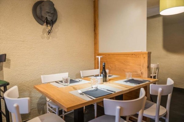 Dřevěný stůl s bílými židlemi v útulné restauraci, na stěně dekorace gorily.
