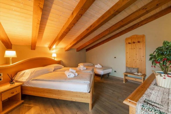 Ložnice s dřevěným nábytkem, velkou postelí a dvěma jednolůžky pod šikmým stropem.