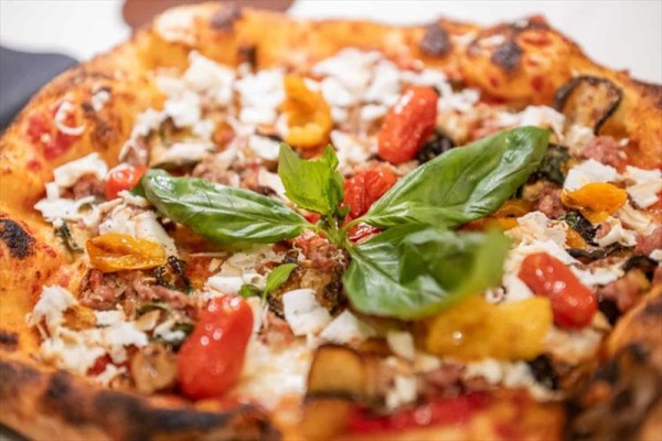 Pizza ozdobená bazalkou, cherry rajčátky a sýrem.