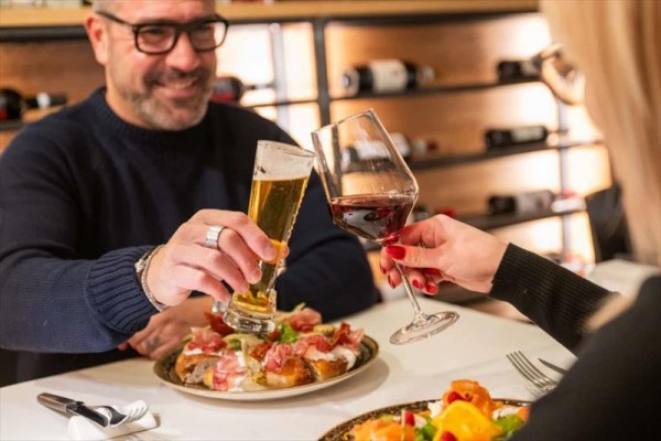 Sklenky vína a piva přiťukávající nad talíři s jídlem v restauraci.