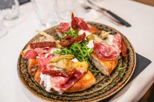 Tarte flambée s prosciuttem, rukolou a sušenými rajčaty na talíři.