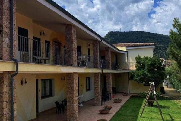 Dvoupodlažní budova s terasami, křesly a travnatým dvorkem na pozadí hor.