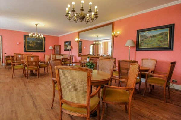 Restaurace s dřevěnými stoly a židlemi, růžovými stěnami a lustry.