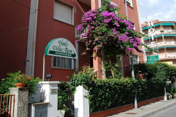 Vchod do hotelu Villa Rosa obklopený kvetoucími rostlinami.