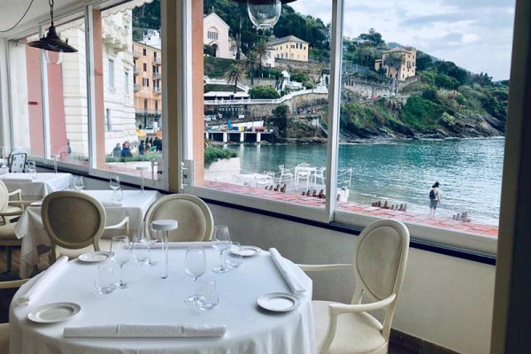 Pohled z restaurace s prostřeným stolem na mořský záliv a pobřeží s budovami.