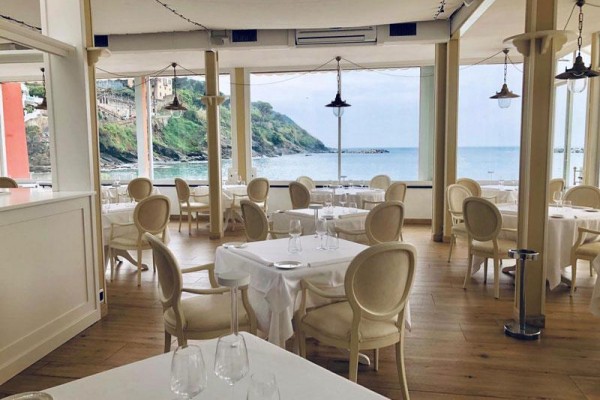 Restaurace s bílými stoly a výhledem na moře a pobřeží.