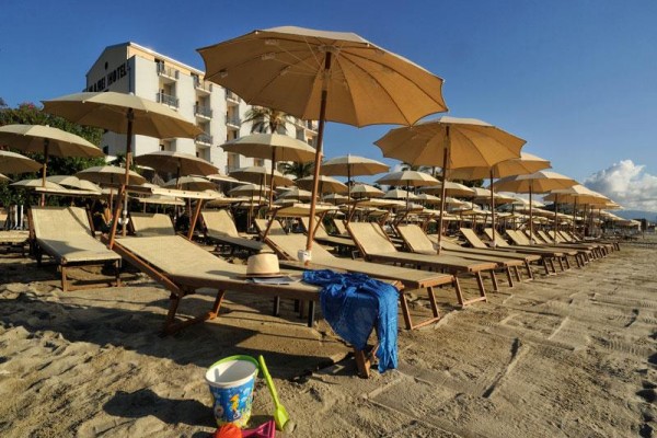 Řada lehátek s hnědými slunečníky na písečné pláži vedle hotelu.