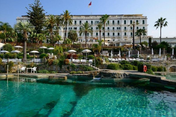 Luxusní hotel s bazénem a palmami v zahradě.