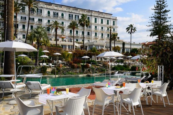 Luxusní hotel s bazénem a venkovními stoly obklopený palmami.