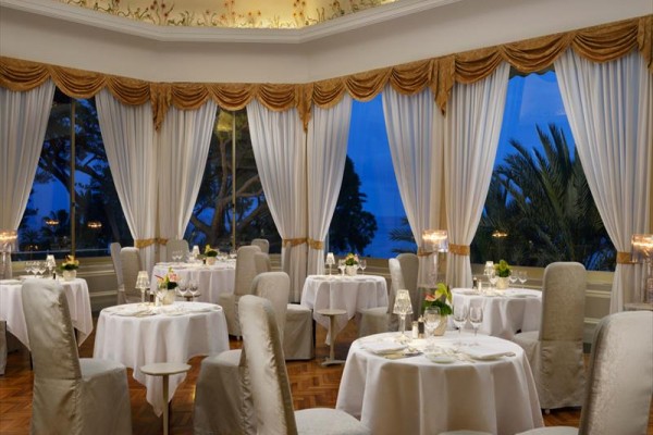 Elegantní restaurace s kulatými stoly, bílými ubrusy a výhledem na večerní krajinu.