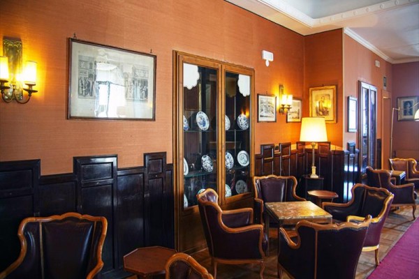 Elegantní salon s koženými křesly, dřevěným obložením a vitrínou s porcelánem.
