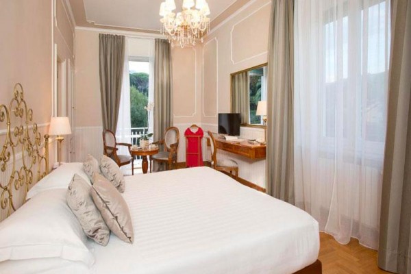 Elegantní ložnice s velkou postelí a křesly u okna s výhledem na zahradu.  