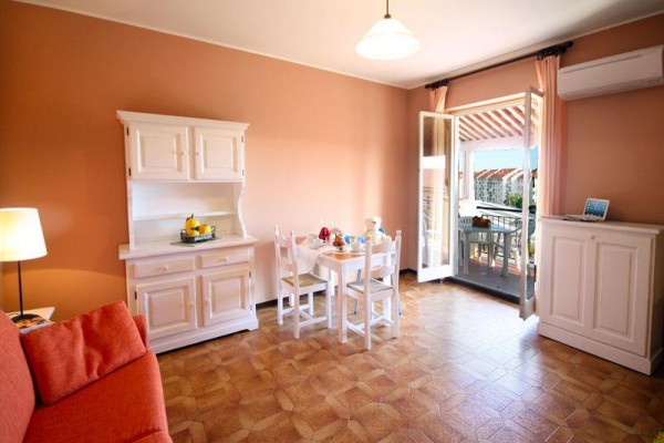 Světlý obývací pokoj s jídelním stolem, bílým nábytkem a otevřenými dveřmi na balkon.