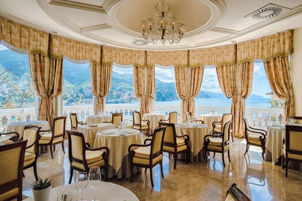 Elegantní restaurace s kulatými stoly a výhledem na moře a hory.