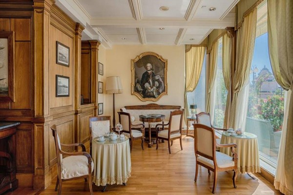 Elegantní kavárna s dřevěným obložením, starožitným nábytkem a obrazem muže na stěně.