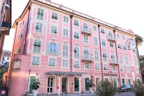 Růžová budova hotelu se zdobenými fasádami a bílými okenicemi.