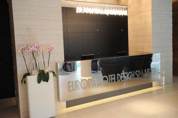 Recepce moderního hotelu s designovým pultem a dekorativními květinami.