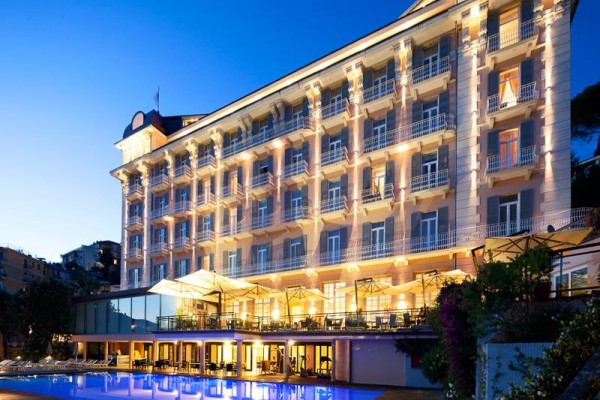Luxusní hotel s osvětlenou fasádou a venkovním bazénem za soumraku.