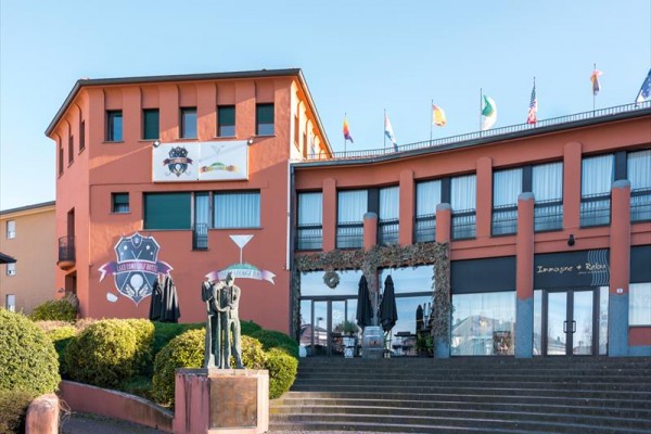 Budova s oranžovou fasádou, zdobená vlajkami na střeše, s venkovním schodištěm a sochou ve spodní části.