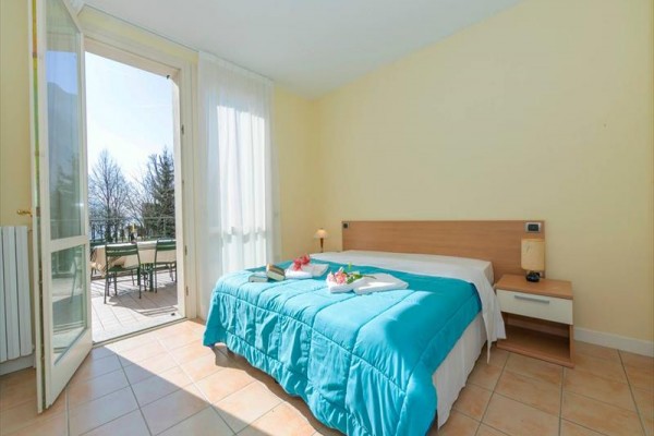 Světlá ložnice s postelí a otevřenými dveřmi na balkon.