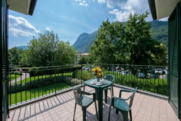 Slunečný balkon s plastovým nábytkem a výhledem na hory a stromy.