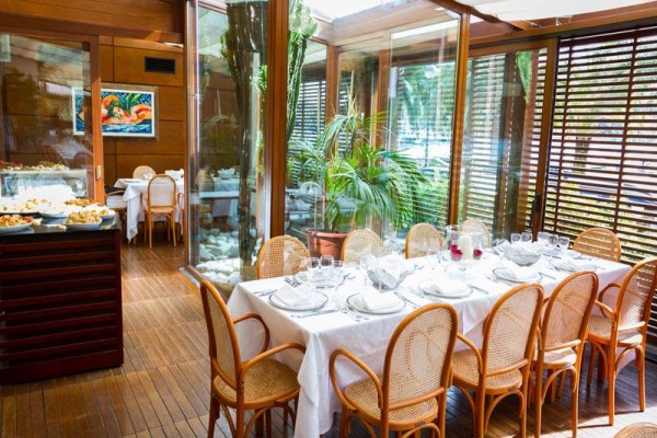 Elegantně prostřený stůl v prosklené restauraci s ratanovými židlemi a výhledem na zeleň.