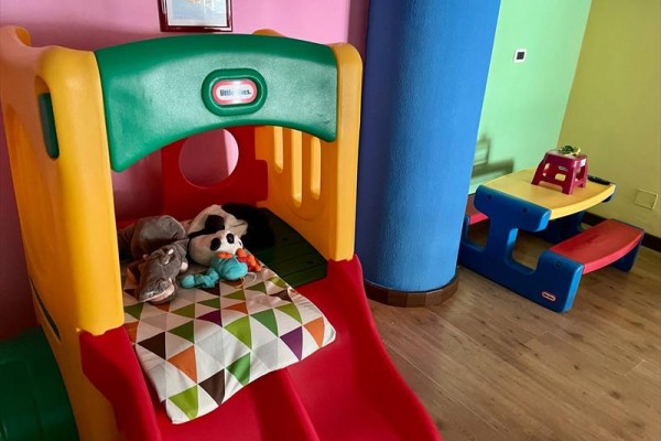 Dětská skluzavka s plyšovými hračkami a barevným stolem v místnosti.