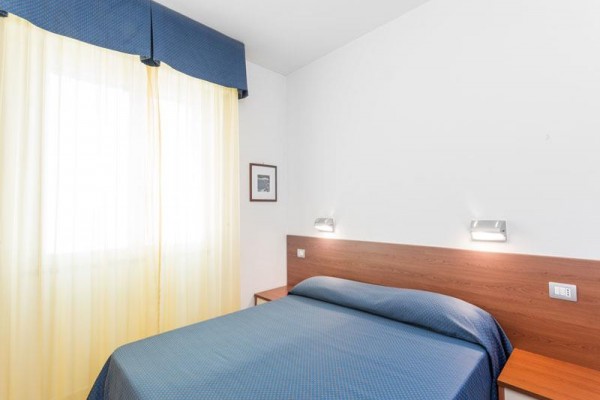 Ložnice s dvojlůžkem, modrým povlečením a žlutými závěsy.