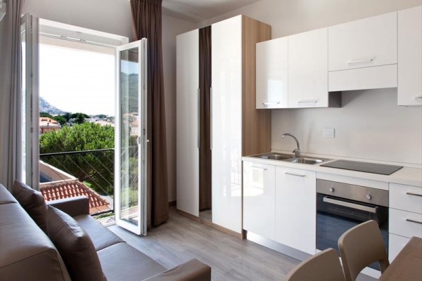 Moderní kuchyně s otevřenými dveřmi na balkon s výhledem na stromy.