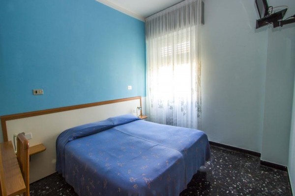 Pokoj s modrou stěnou a manželskou postelí pod oknem.
