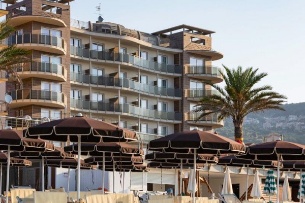 Moderní hotel s balkony a palmy před ním.  