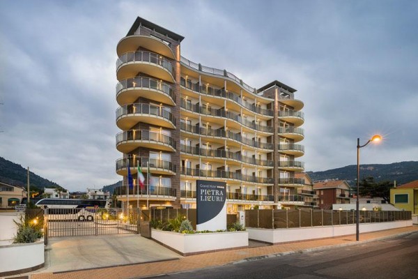 Moderní vícepatrový hotel s balkony a skleněnými zábradlími za šera.