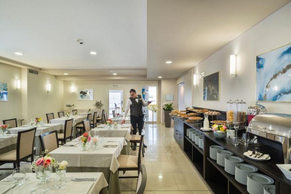 Restaurace s ubrusy na stolech a servírovacím bufetem, kde obsluha upravuje stůl.  