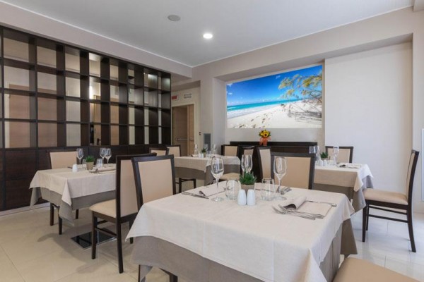 Moderní restaurace s prostřenými stoly a plážovým obrazem na stěně.