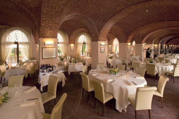 Elegantní restaurace s klenutým cihlovým stropem a kulatými stoly s bílými ubrusy.