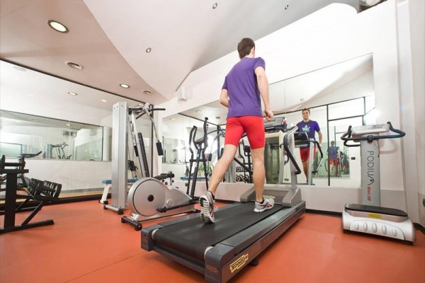 Muž cvičící na běžeckém pásu ve fitness centru.