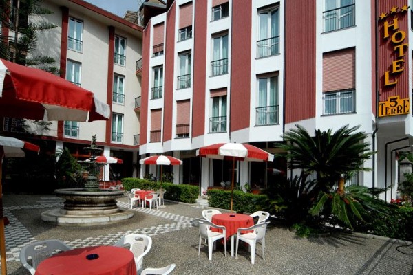 Venkovní terasa hotelu s červenobílými slunečníky, stoly a plastovými židlemi.