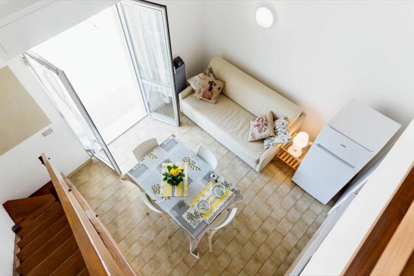Přehled obývacího pokoje s pohovkou, jídelním stolem a otevřenými dveřmi na balkon.